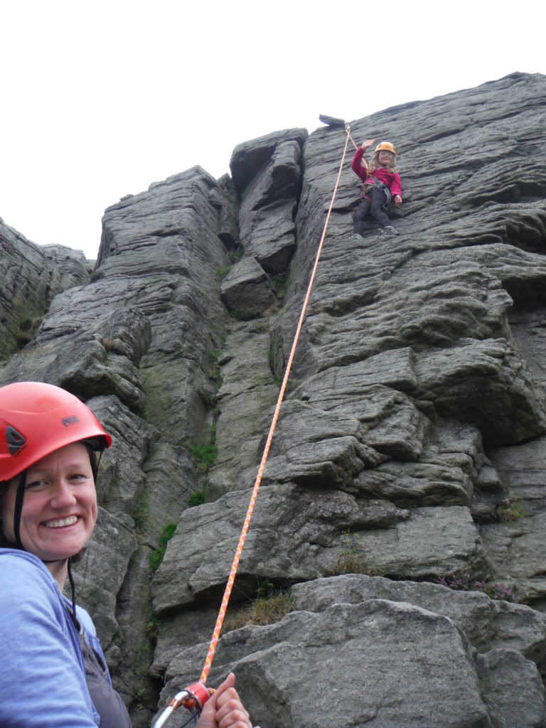 A child climbing smiles to the camera while mum holds the rope