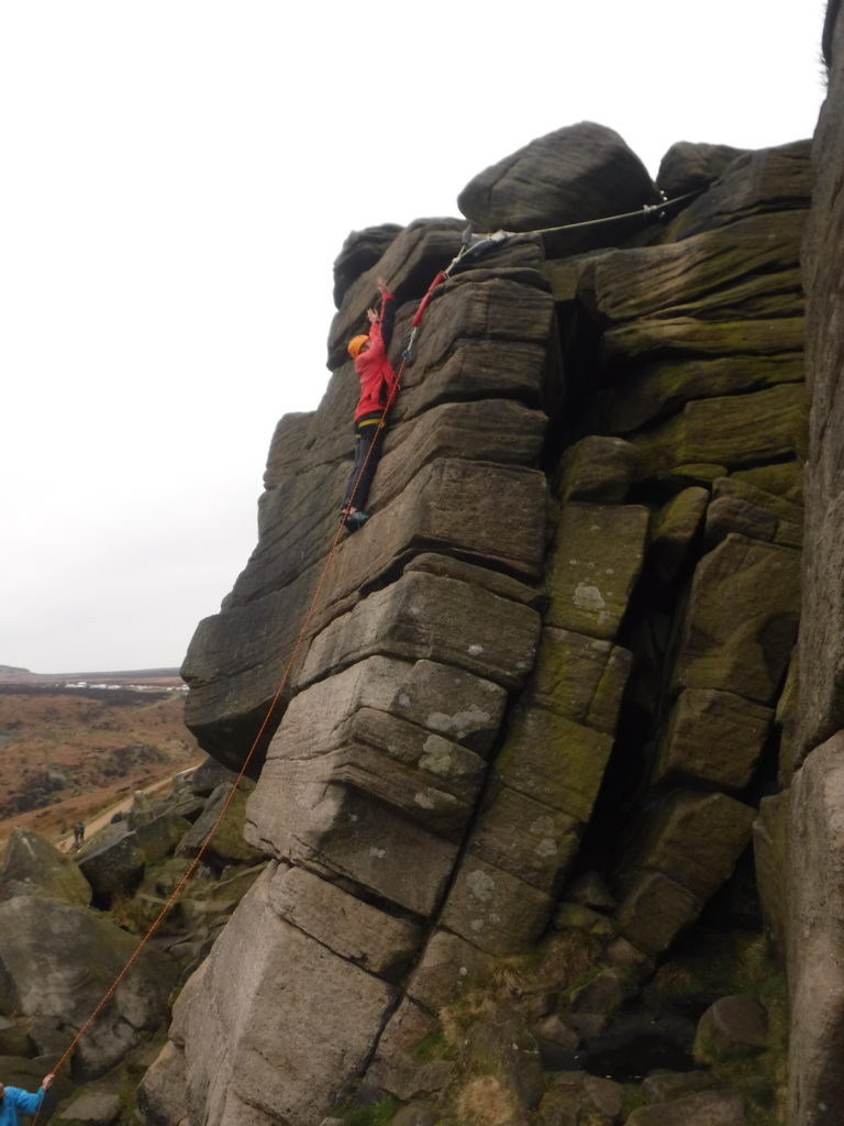 A rock climber reaching for the top of a steep cliff