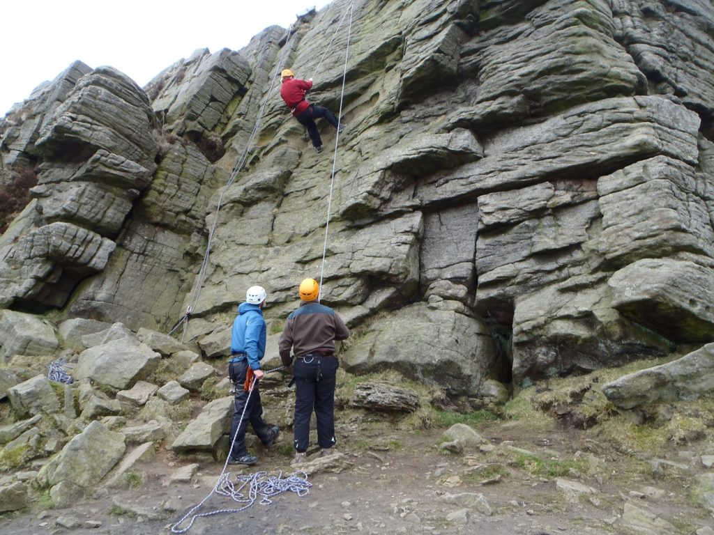 A rock climber is lowered from the cliff by another climber and the instructor